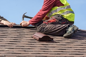 man nailing shingles to roof