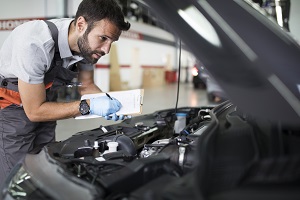 mechanic looking under hood of car writing on a clipboard
